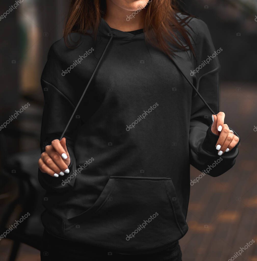 Design mock-up for clothing logo on a black pullover. A young woman wears a black hoodie on the street.