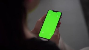 Oturma odasındayken bir kız telefonunu tutuyor. Tek eliyle akıllı telefon kullanan bir kadına yaklaş. Anahtar için yeşil ekran modellemesi.