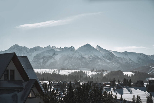 Distant winter mountain ridge panorama with rocky peaks. Dramatic view of mountains with snow-covered summit. Polish tatry in winter.
