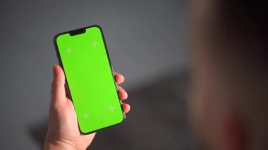 Bir adamın eli dikey ekranı görünen bir akıllı telefonu tutuyor. Adam elinde yeşil ekranlı bir cep telefonu tutuyor.