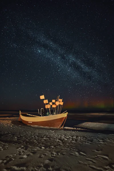 Abandoned boat at the baltic seashore with Milky way and northern lights in the background. Concept of travel destination. Long exposure night sky photo.