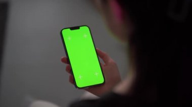 Oturma odasındayken bir kız telefonunu tutuyor. Tek eliyle akıllı telefon kullanan bir kadına yaklaş. Anahtar için yeşil ekran modellemesi.