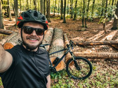 Ormanda kask ve güneş gözlüğü takan bir bisikletçinin selfie 'si. Dışarıda bisiklet sürerken gülümseyen bir adam. Kırsal bölgelerde bisiklet sürerken güvenlik kavramı