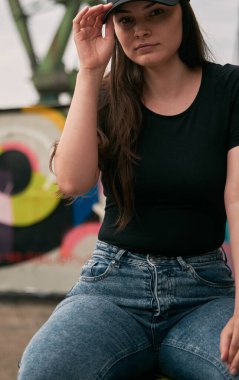 Esmer siyah bir tişört giyiyor. Tasarımcılar koyu renk gömlek için modellik yaparlar. Güzel manken kız şehirde açık havada logo giymez..