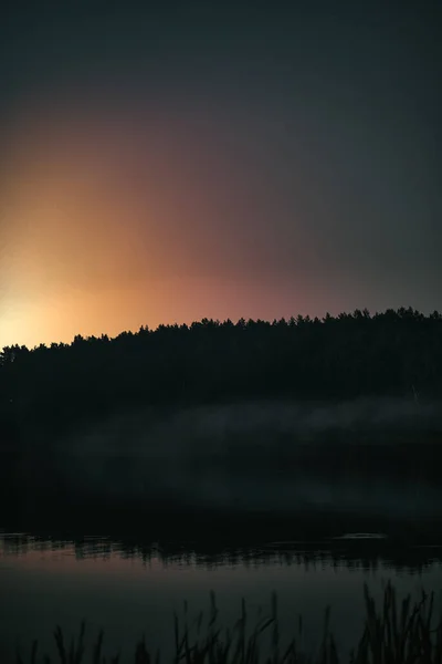 Night at the lake. Smoke on the water during the late evening. Forest reflection in the water with mist.