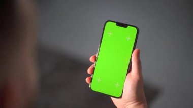 Bir adamın eli dikey ekranı görünen bir akıllı telefonu tutuyor. Adam elinde yeşil ekranlı bir cep telefonu tutuyor.