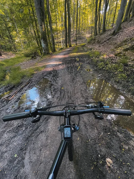POV photo of riding a bicycle on the forest muddy path. Close up of a bike handlebar with a forest background. Concept of extremely rural and outdoor bike riding.