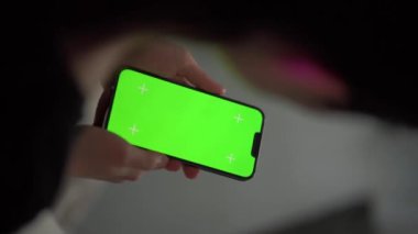 Oturma odasındayken bir kız telefonunu tutuyor. Tek eliyle akıllı telefon kullanan bir kadına yaklaş. Anahtar için yeşil ekran modellemesi.