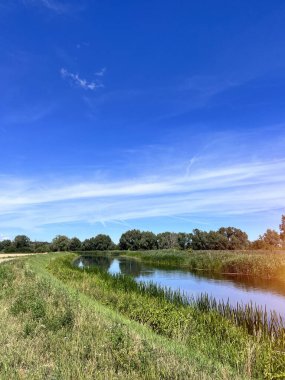 Summer rural river landscape on a sunny day. Countryside panorama with grass, trees and sky in Europe.