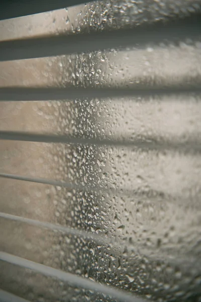 Raindrops on a window with an apartment house background. Concept of staying home while there is bad weather outside. Cozy indoor view at rainy weather