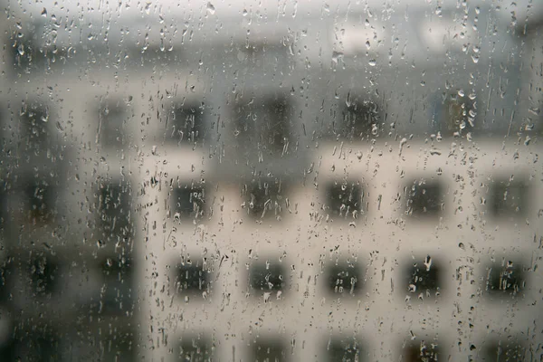 Rain droplets on the window glass. View from the window at the blurred street with buildings during bad weather.