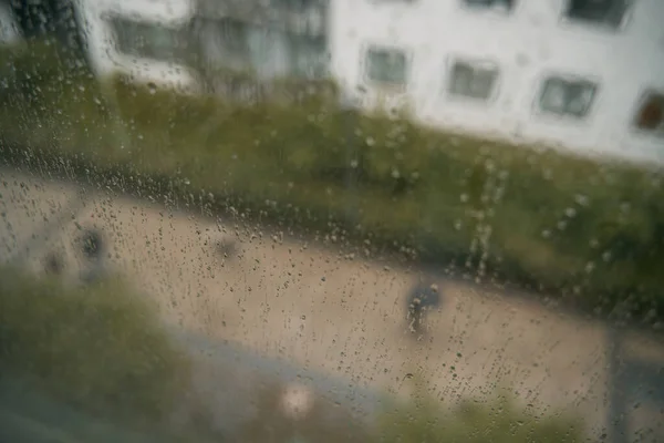 Raindrops on a window with an apartment house background. Concept of staying home while there is bad weather outside. Cozy indoor view at rainy weather