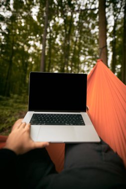 POV of a Tourist working remotely with Laptop Computer. Traveller Resting in a hammock in the forest. Adventurous Hiker Living in Nature.