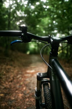 Bicycle frame, air suspension fork and handlebar with brake handle with forest background. Concept of using MTB on a path in the woods.