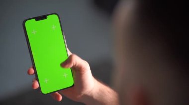 Bir adamın eli dikey ekranı görünen bir akıllı telefonu tutuyor. Adam elinde yeşil ekranlı bir cep telefonu tutuyor.