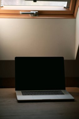 Uzaktan çalışma ve içeride dizüstü bilgisayar kullanma kavramı. Tahta bir masada dizüstü bilgisayar, boş bir bilgisayar ekranı. İskandinav iç ve çatı penceresi.