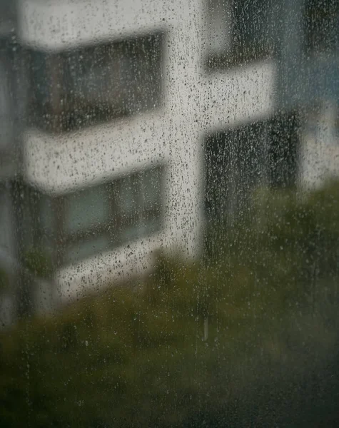 Rain droplets on the window glass. View from the window at the blurred street with buildings during bad weather.