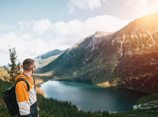 旅行的人微笑着 背后是山清水秀的湖水和森林 户外探险和徒步旅行的概念 在山上 留着胡子的年轻的高加索男子身穿背包和运动服 — 图库照片