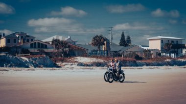 Daytona Beach, Florida, ABD - 17 Aralık 2021: Olgun beyaz bir çift lüks evleri ve arka planda güzel mavi gökyüzü olan plajlarda bisiklet sürüyor