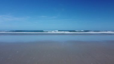 Alçak uçakla kumlu sahile doğru itin ve derin mavi gökyüzü ile yumuşak sörf yapın. Dramatik yükseliş ile havadan 4k çekim.