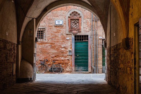 Lucca, Italy - 6/8/2022: Bicycle at rest in traditional Tuscan courtyard in Lucca, Italy.