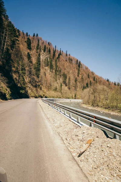 Bergsväg problem flod, blandskog och staket Stockbild