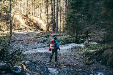 Dağlarda taşlarla dolu bir nehir, bir turist nehri geçiyor.