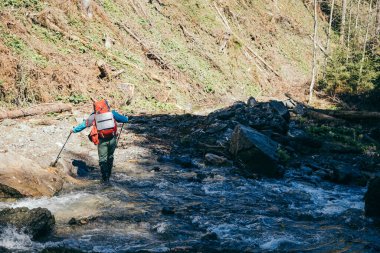 Dağlar, nehir, sırt çantalı turist nehri geçiyor.