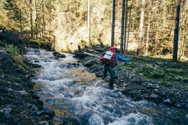 Dağlarda taşlarla dolu bir nehir, bir turist nehri geçiyor.