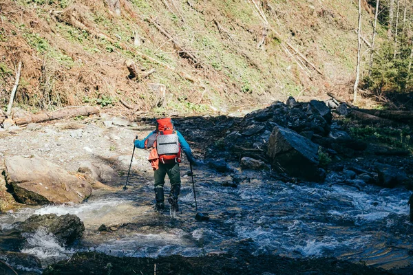 Montagne, fiume, turista con uno zaino attraversa il fiume — Foto Stock