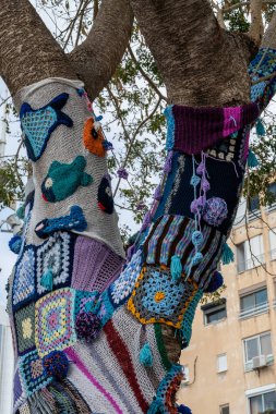 Ağaç gövdesi bombalamasına renkli örgü örülmüş. Sıcaklık, koruma ve dekorasyon için yamalı örgü örülmüş ağaç. Yüksek çözünürlük