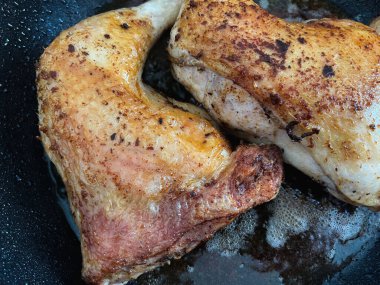 İki tavuk bacağı büyük miktarda yağda tavada kızartılır. Yakın plan..