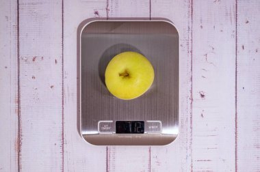 Bir elma, ışık panolarının üzerinde dijital bir mutfak terazisinde yatıyor. en üstteki görünüm.