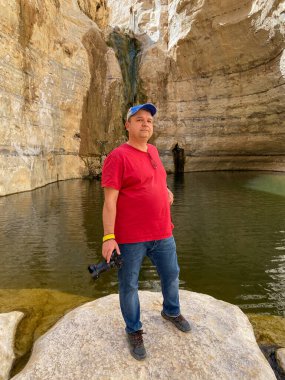 İsrail 'deki Ein Avdat Kanyonu' nda elinde kamera olan bir adam şelalenin önünde duruyor. Dağlarda manzaralar.