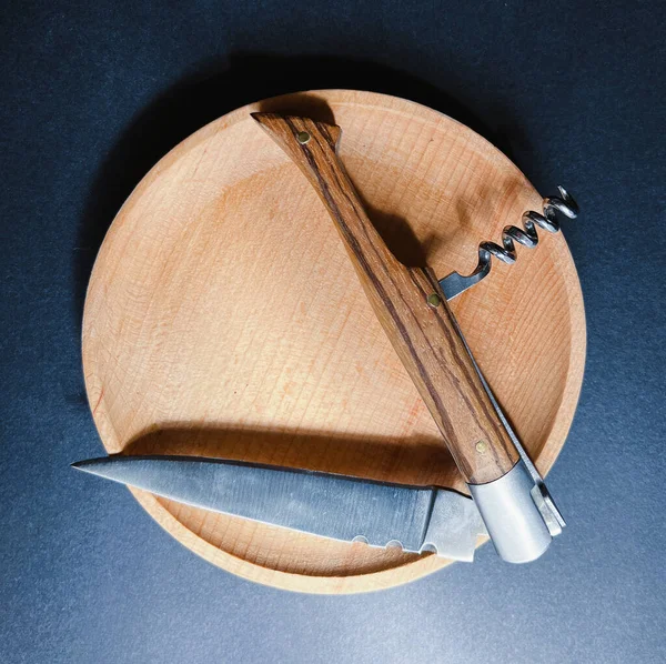An open pocket folding knife with a corkscrew lies on a wooden plate. Close-up.