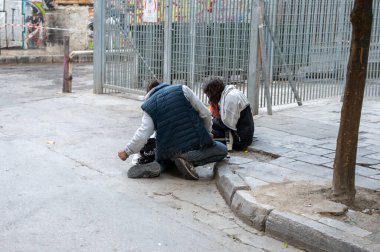 ATHENS, GREECE - MAY 14, 2022: A homeless man sleeps on a sidewalk in downtown Athens. Tourists pass by.