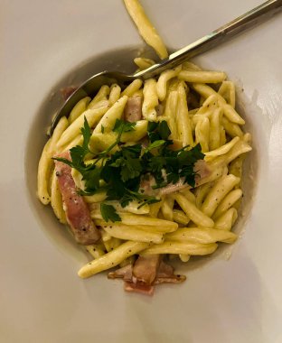 Pasta Carbonara is placed on a white plate with a large margin. Topped with herbs. View from above.