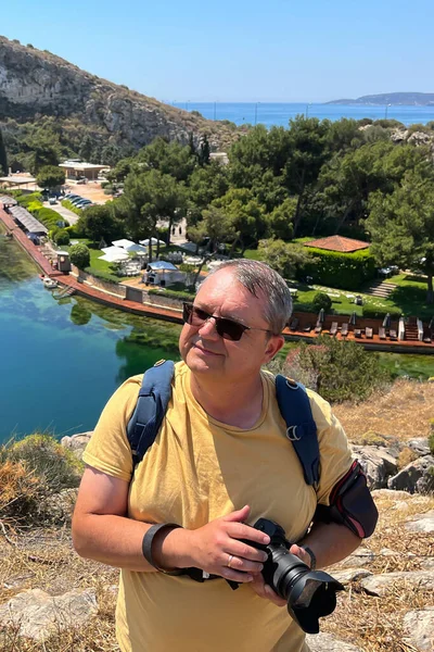 A man with a camera on the background of the volcanic lake Vouliagmeni with azure water and radon, located 25 km from the center of Athens and 100 meters from the sea. Sunny day.