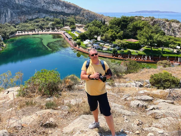 A man with a camera on the background of the volcanic lake Vouliagmeni with azure water and radon, located 25 km from the center of Athens and 100 meters from the sea. Sunny day.