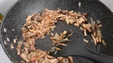 Shimeji mushrooms are fried in a pan with onions. Close-up.