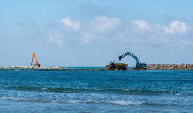 Bir kazıcı ve bir maden kamyonu taşları denize taşır. Netanya, İsrail 'de sahili korumak için dalgakıran inşaatı. Endüstriyel yapı ekipmanı ve makineleri.