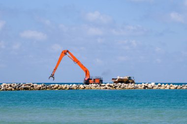 Bir kazıcı ve bir maden kamyonu taşları denize taşır. Netanya, İsrail 'de sahili korumak için dalgakıran inşaatı. Endüstriyel yapı ekipmanı ve makineleri.
