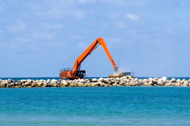 Bir kazıcı ve bir maden kamyonu taşları denize taşır. Netanya, İsrail 'de sahili korumak için dalgakıran inşaatı. Endüstriyel yapı ekipmanı ve makineleri.