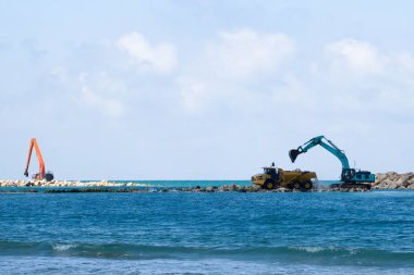 Bir kazıcı ve bir maden kamyonu taşları denize taşır. Netanya, İsrail 'de sahili korumak için dalgakıran inşaatı. Endüstriyel yapı ekipmanı ve makineleri.