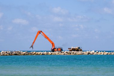 Bir kazıcı ve bir maden kamyonu taşları denize taşır. Netanya, İsrail 'de sahili korumak için dalgakıran inşaatı. Endüstriyel yapı ekipmanı ve makineleri.