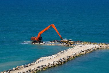 Bir kazıcı ve bir maden kamyonu taşları denize taşır. Netanya, İsrail 'de sahili korumak için dalgakıran inşaatı. Endüstriyel yapı ekipmanı ve makineleri.