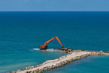 Bir kazıcı ve bir maden kamyonu taşları denize taşır. Netanya, İsrail 'de sahili korumak için dalgakıran inşaatı. Endüstriyel yapı ekipmanı ve makineleri.