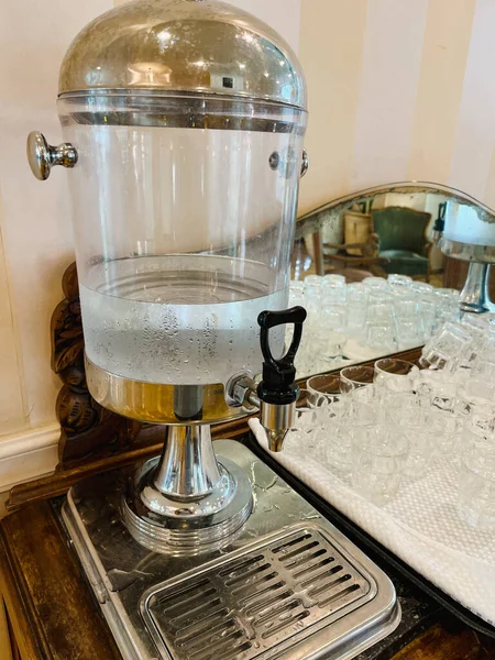 A glass transparent tank with a tap with cold drinking water stands in the hotel lobby. Close-up.