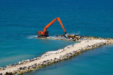 Bir kazıcı ve bir maden kamyonu taşları denize taşır. Netanya, İsrail 'de sahili korumak için dalgakıran inşaatı. Endüstriyel yapı ekipmanı ve makineleri.