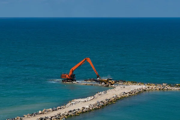 Bir kazıcı ve bir maden kamyonu taşları denize taşır. Netanya, İsrail 'de sahili korumak için dalgakıran inşaatı. Endüstriyel yapı ekipmanı ve makineleri.